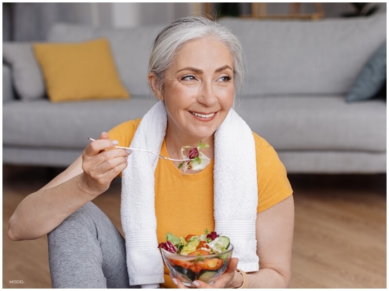 A senior woman smiling after a workout, eating a healthy meal. Her confident posture reflects her commitment to health and well-being