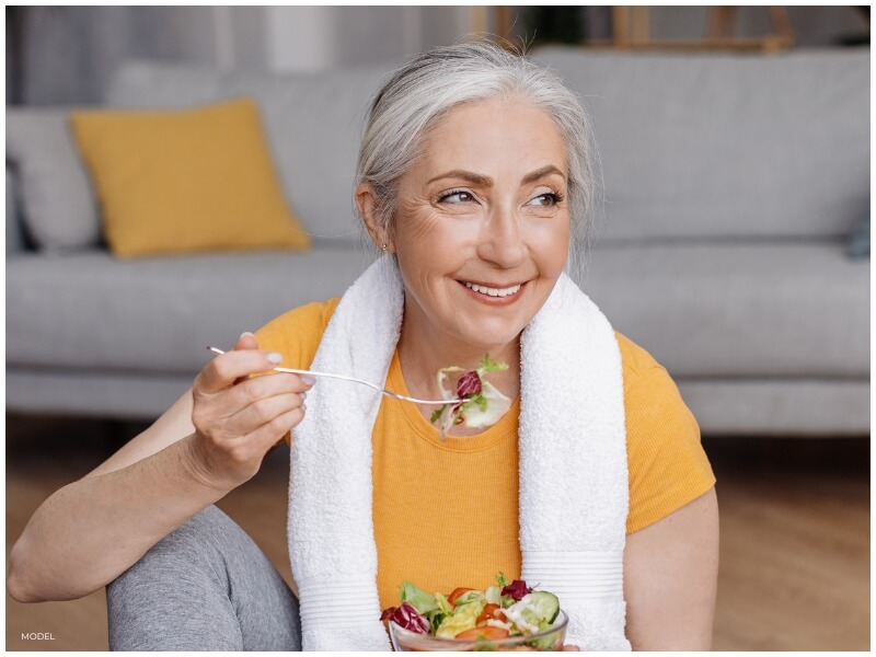 Woman eating healthy fruits and vegetables promoting a nutritious diet for maintaining facelift outcomes.