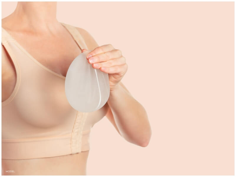 woman holding breast implant next to sizing bra