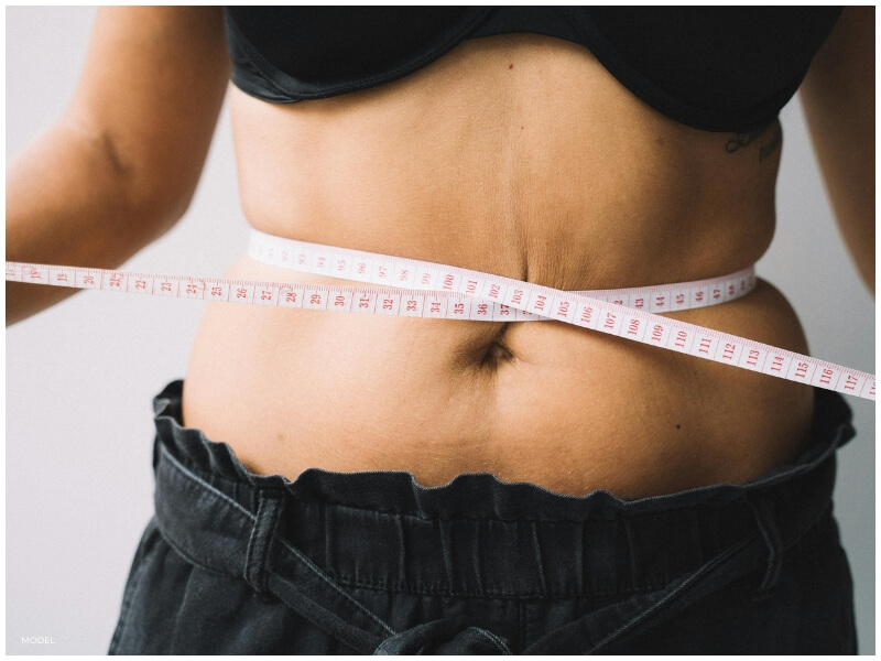 A fit woman checking her abdominal contour, indicative of someone considering a tummy tuck for body confidence.