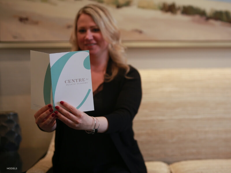 woman in the lobby of centre for plastic surgery holding a brochure about liposuction in the office