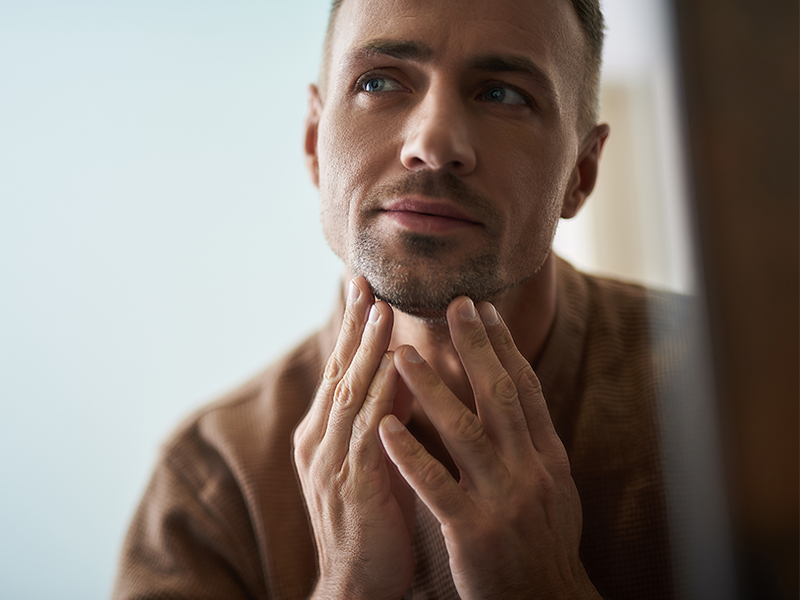man considering his face in the mirror contemplating facial plastic surgery for men